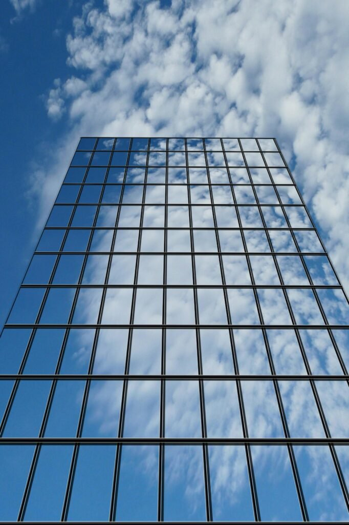 Low angle shot of a modern glass building reflecting clouds and blue sky.